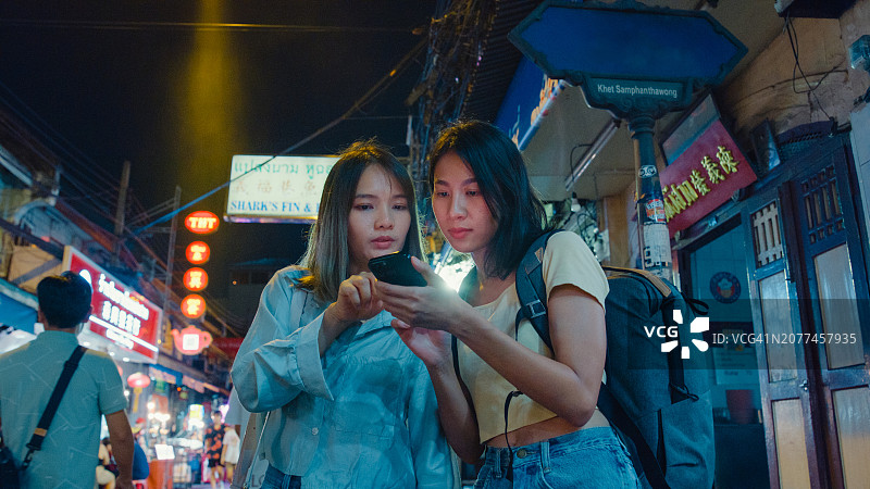 年轻的亚洲女性朋友在泰国曼谷的夜晚街头使用手机图片素材