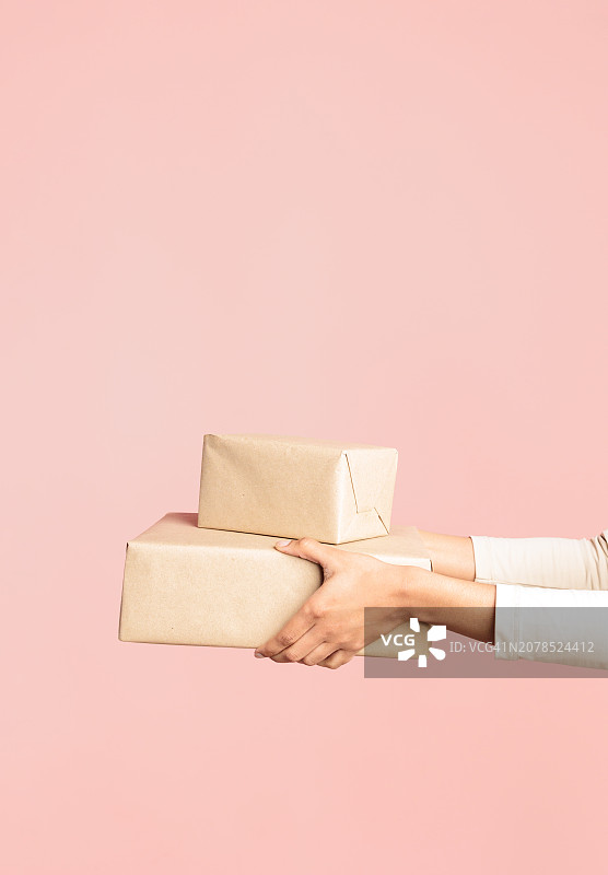 女人拿着棕色纸箱，漂浮在粉色背景上图片素材