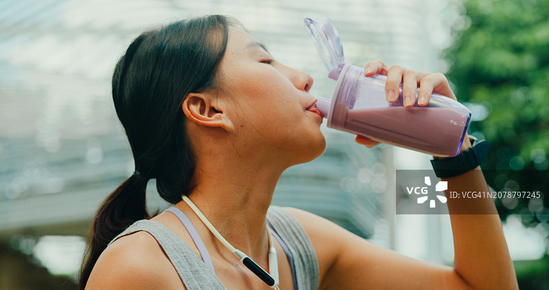 年轻亚洲女运动员在城市公园锻炼后饮用蛋白奶昔特写图片素材