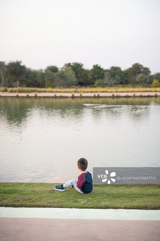男孩坐在水边的草地上图片素材