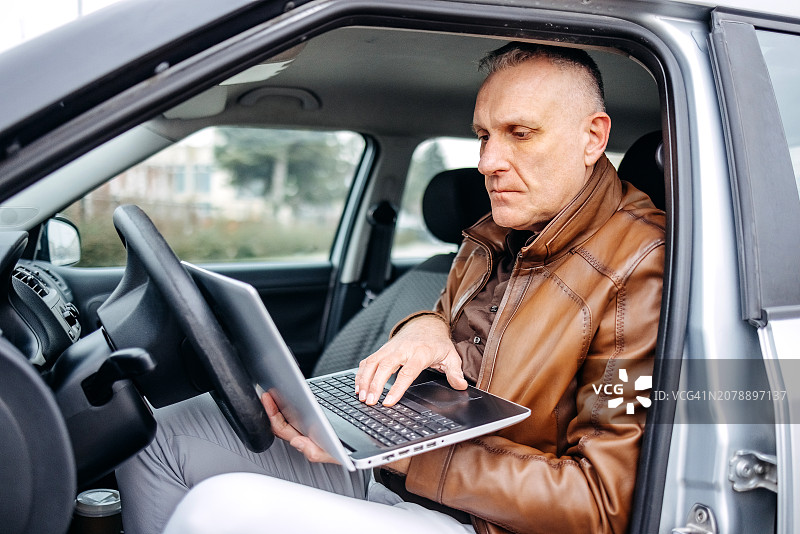 男人开车上班并在笔记本电脑上工作图片素材