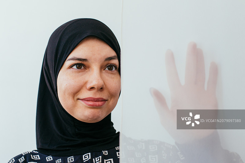 一位戴着黑色头巾的年轻迷人穆斯林女孩在窗帘后图片素材