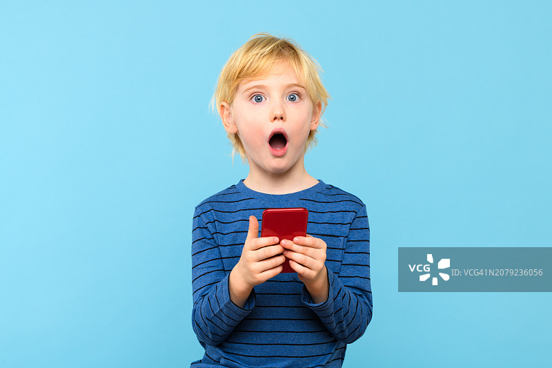 震惊的男孩肖像，手拿手机蓝色背景图片素材