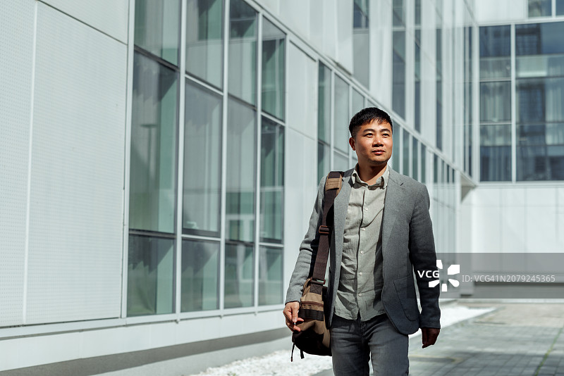 衣着得体的年轻商人走在现代建筑前图片素材