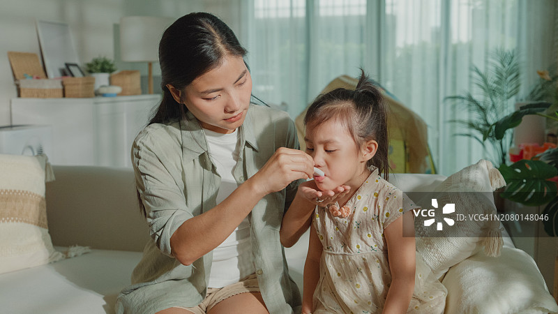 妈妈在家照顾发烧感冒的女儿，给孩子喂药，呵护生病的孩子，关注家庭健康图片素材