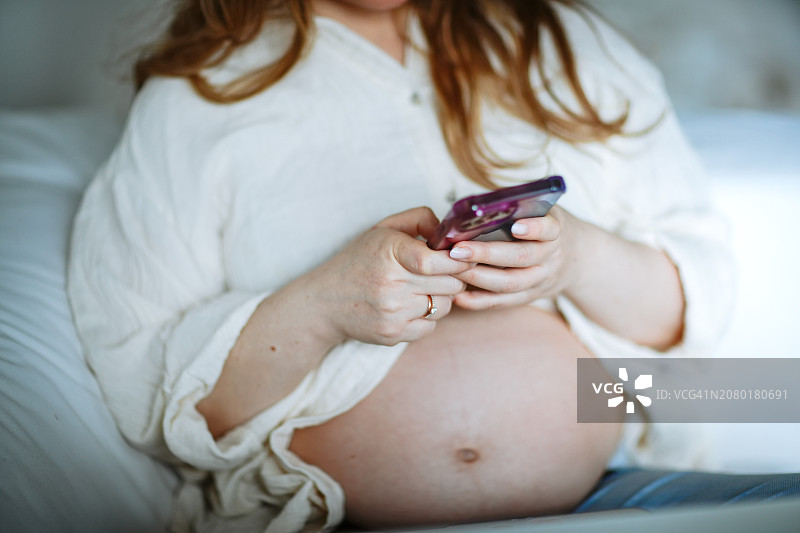 中年孕妇坐在沙发上使用智能手机，浅色图像图片素材