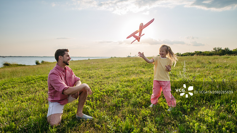 日落时分，父女在草地上玩轻型泡沫飞机。有趣的爸爸和女儿扔掷和放飞泡沫滑翔机图片素材