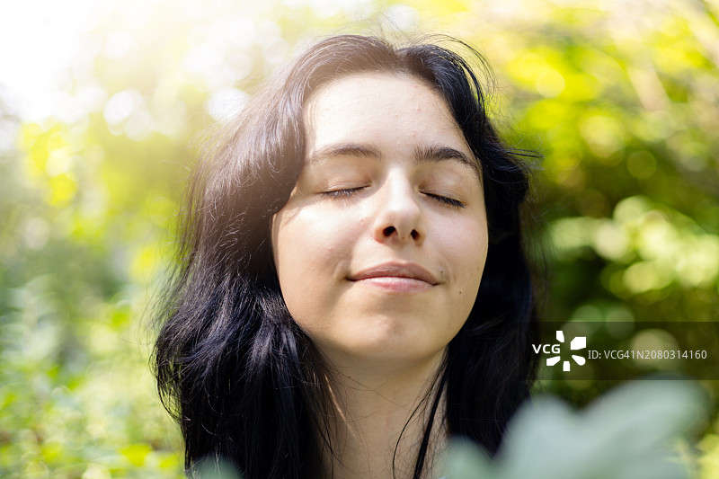 享受户外阳光的年轻漂亮棕发女子。在绿色大自然中微笑的平和女孩图片素材