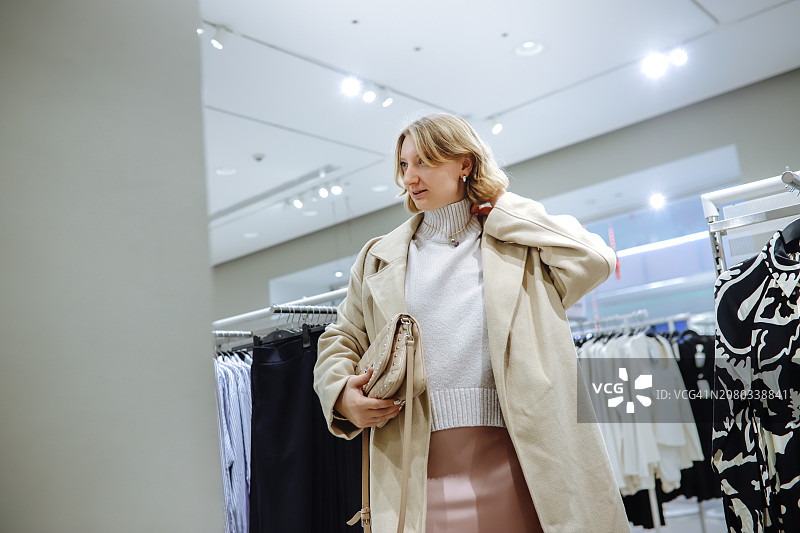 日常时尚选择：金发女人在服装店挑选外套，强调选择时尚外套的重要性图片素材