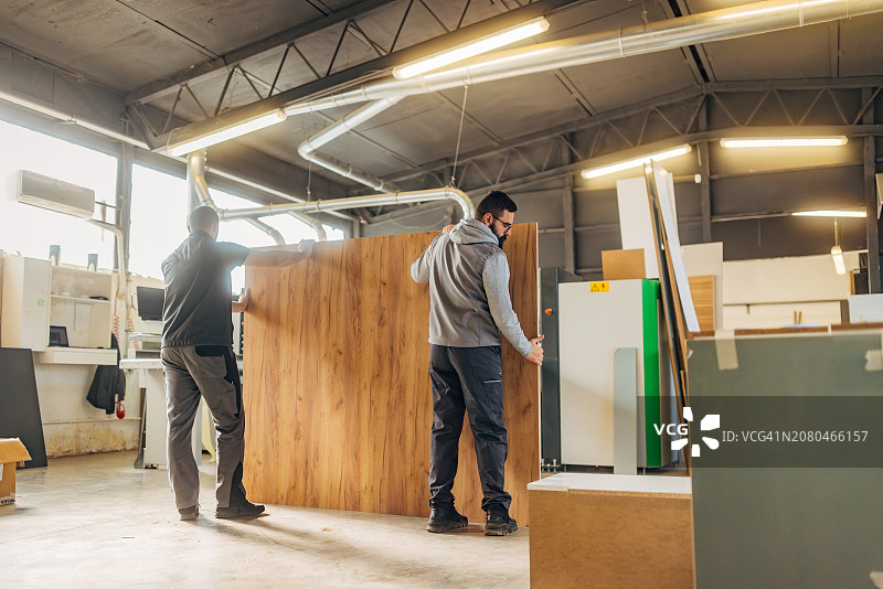 两位经验丰富的木匠在家具制作车间合作，准备刨花板以进行加工图片素材