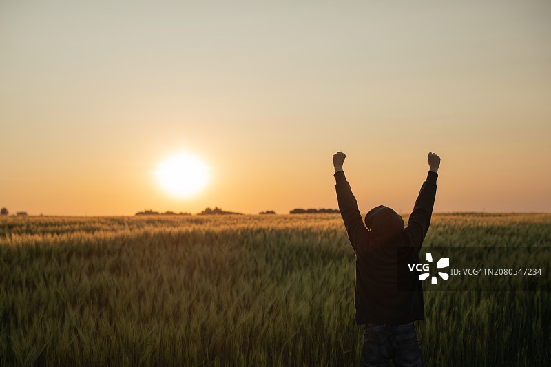 日落时分，男子站在白俄罗斯田野中，举起双臂的背影轮廓图片素材