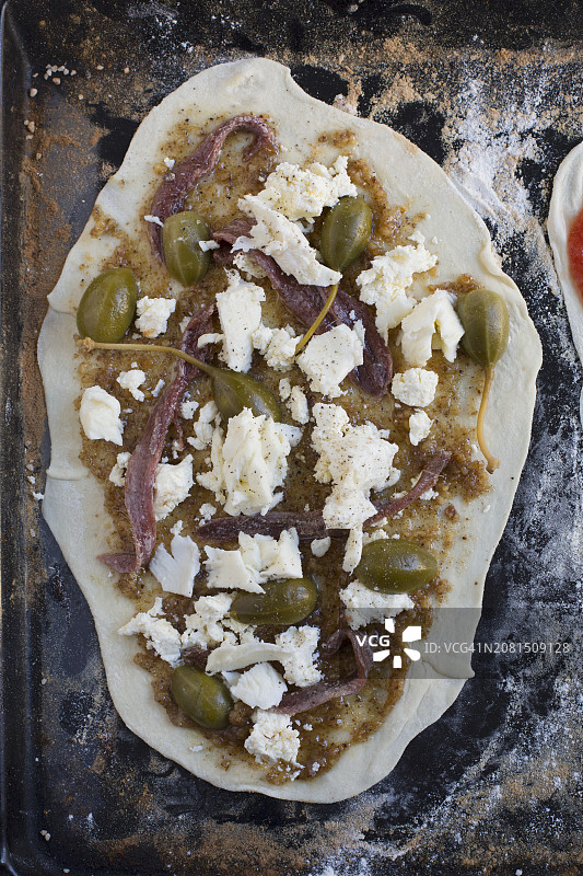 烤盘上的自制披萨配马苏里拉奶酪、刺山柑果、核桃香蒜酱和柠檬沙丁鱼（未烘烤）图片素材