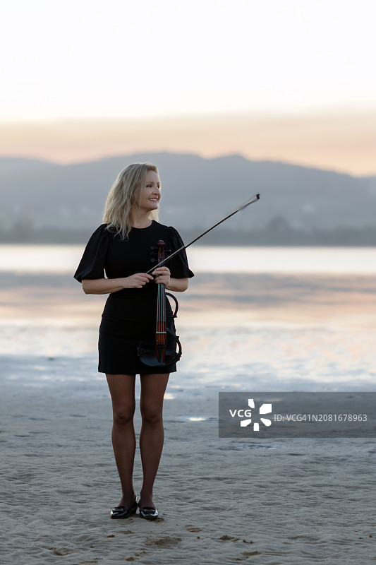 海滩日落时分，手持小提琴的金发艺术家图片素材