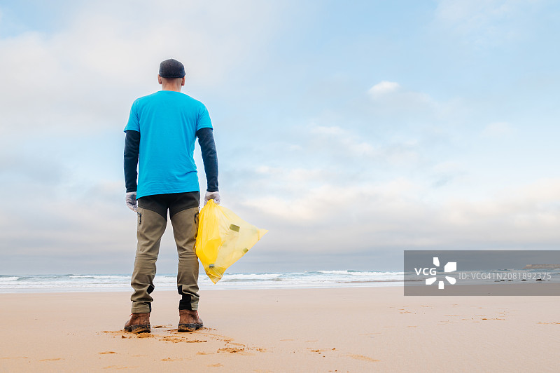 手提黄色垃圾袋的沙滩清洁志愿者图片素材