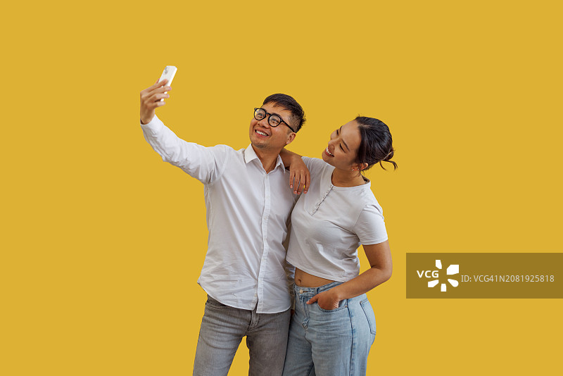 年轻的亚洲情侣在黄色背景前自拍图片素材
