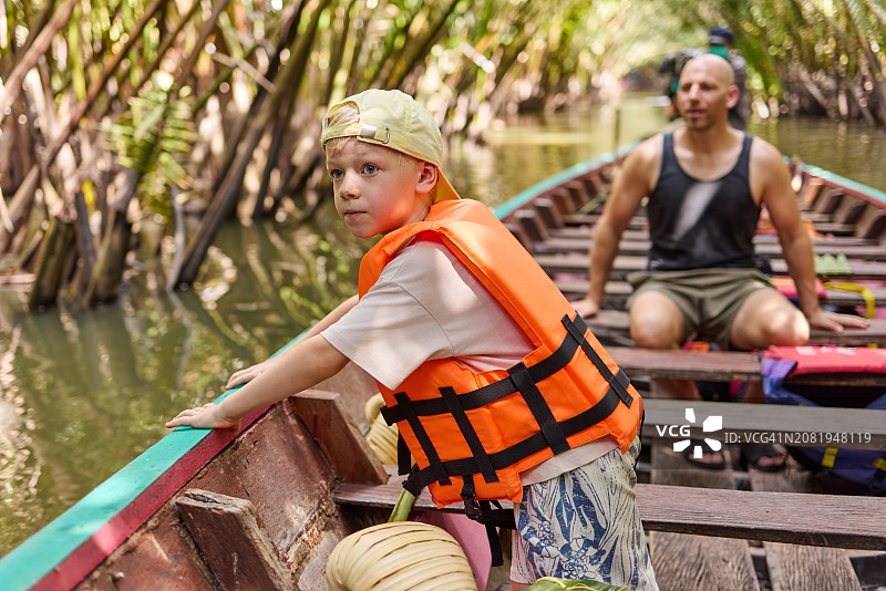 小男孩穿着救生衣坐在长尾船上图片素材