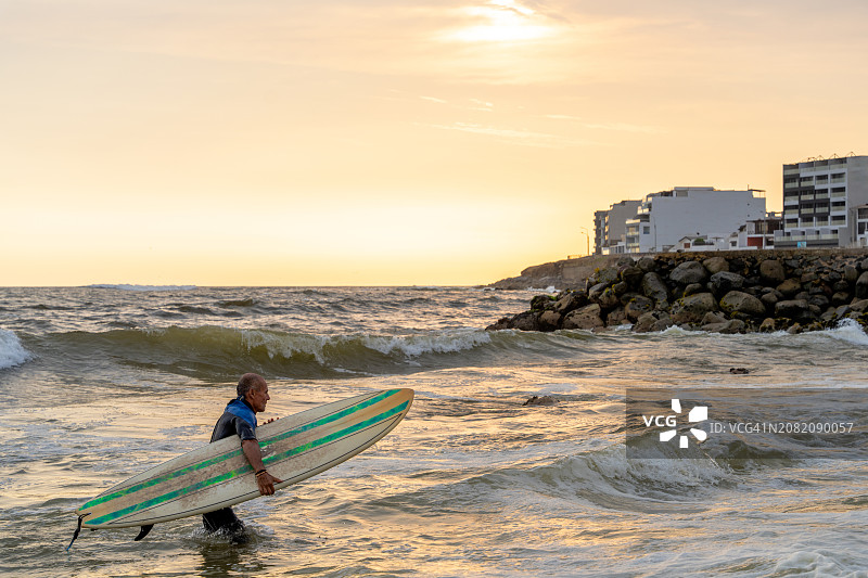 年长的男人带着冲浪板从海里出来图片素材
