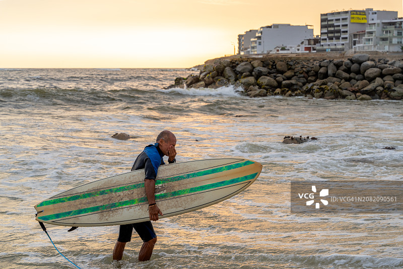 成年男子日落时扛着冲浪板从海里出来图片素材