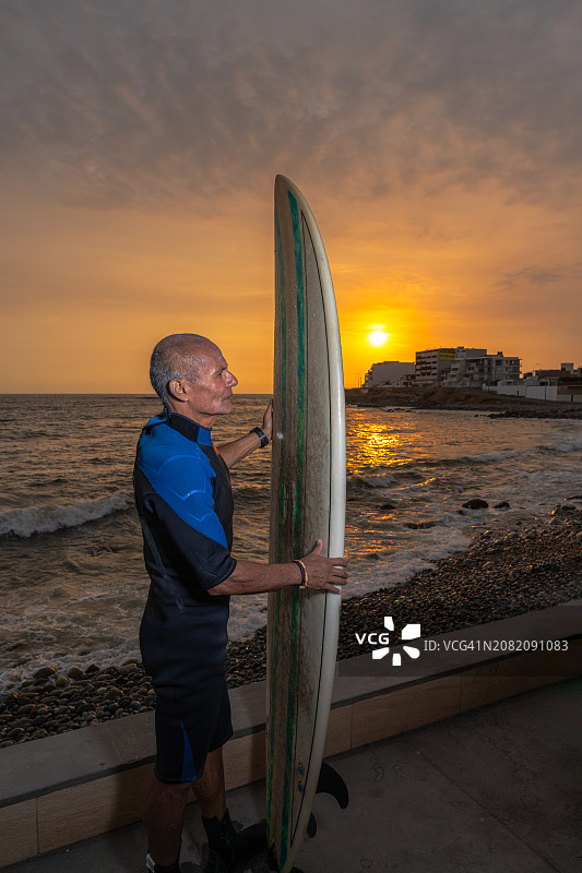 日落时分带着冲浪板的老年男人图片素材