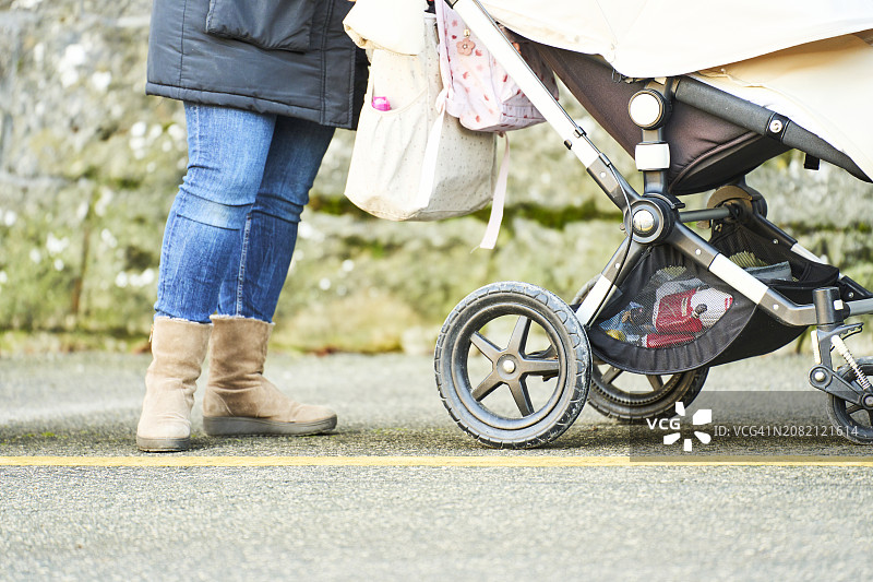 穿着冬装的女人在公园里用婴儿车推着她的宝宝散步图片素材