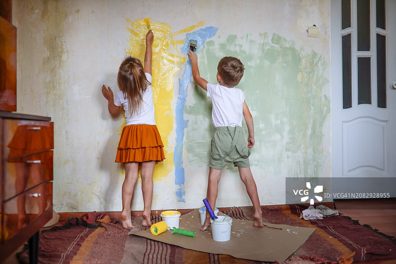 童年乐趣：孩子们用画笔将墙壁涂成黄绿色，表达无限创意图片素材