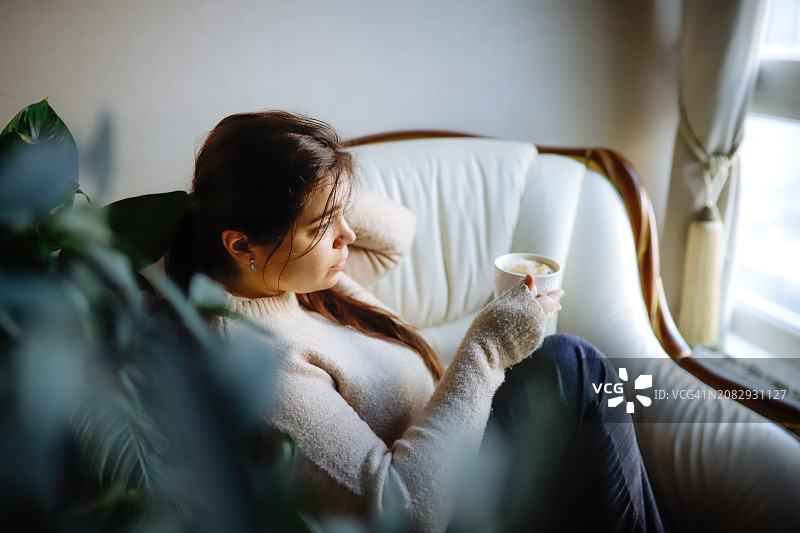 疲惫：曲线女士穿着毛衣，手持咖啡杯，在扶手椅上休息，表现出倦怠和沮丧图片素材