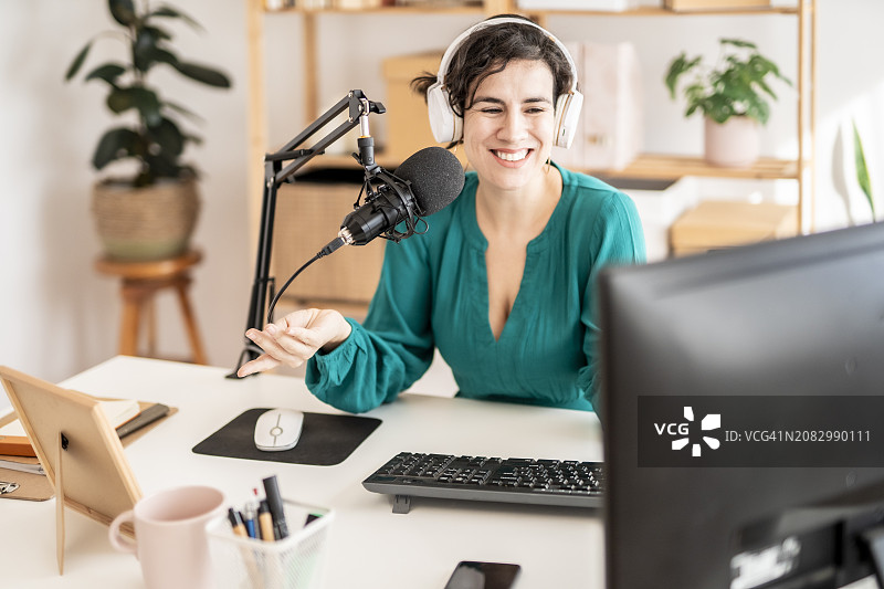 面带微笑的中年妇女在桌前使用麦克风和无线耳机录制播客图片素材