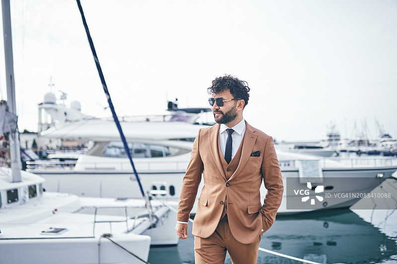 码头边的精致：穿着定制棕褐色西装的温文尔雅的男人自信地在码头上漫步图片素材