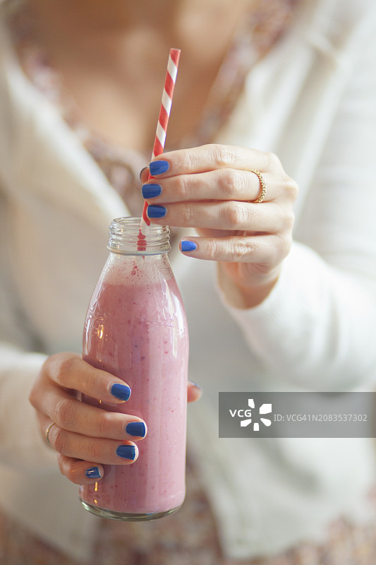 一个女人拿着一杯玻璃瓶装的纯素覆盆子奶昔图片素材