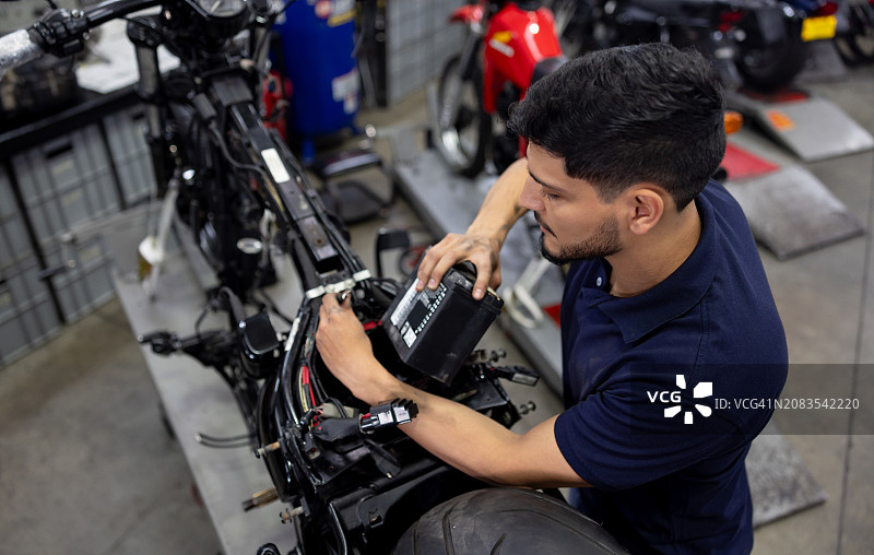 技工在修理店将电池安装在摩托车上图片素材