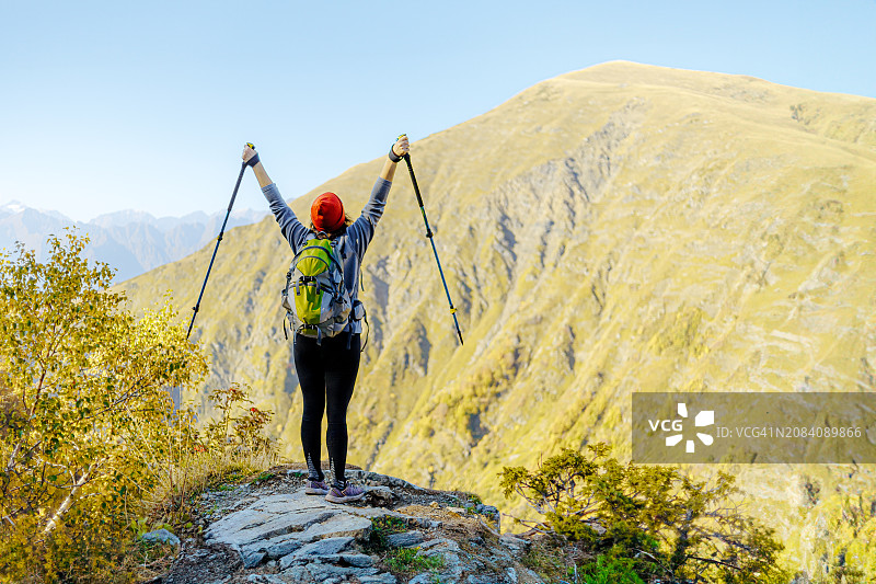 戴着橙色无檐小便帽的徒步旅行者在山区地形中使用登山杖徒步旅行图片素材