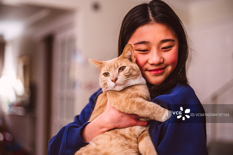 快乐的青少年女孩在家和她的姜黄色虎斑猫拥抱图片素材