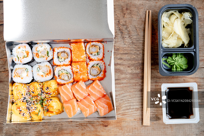 готовые роллы и красная рыба, рис и авокадо в коробке, деревянные палочки, имбирь и васаби на деревянном фоне. Доставка роллов в ассортименте: Филадельфия, Калифорния, классика и запеченные.图片素材