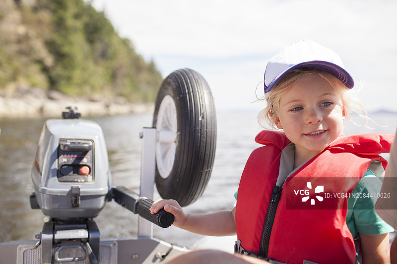 穿着救生衣的年轻女孩在海湾学习驾驶带舷外发动机的小艇图片素材