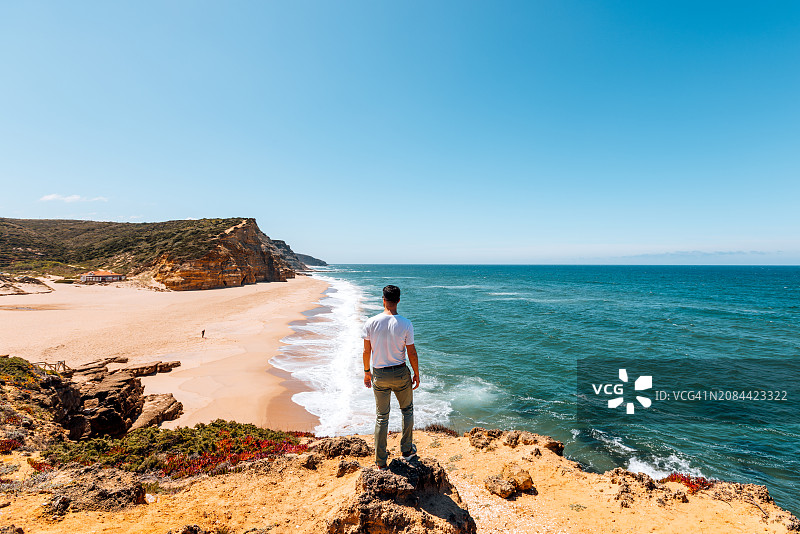 男子站在葡萄牙辛特拉悬崖上俯瞰海滩的背影图片素材