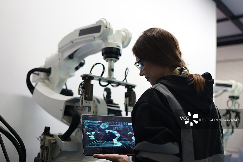 在焊接工厂质检室使用机械臂原型检查新程序的女机械电子工程师图片素材