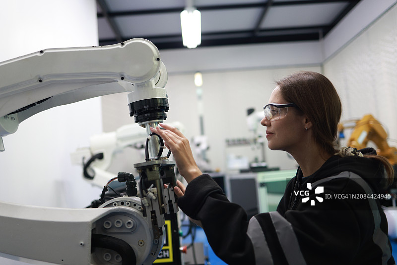 在焊接工厂质检室使用机械臂原型检查新程序的女机械电子工程师图片素材