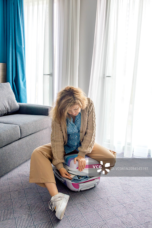 女子坐在行李箱上，努力关上箱子图片素材