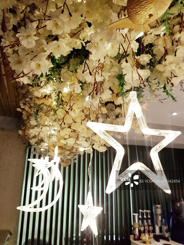 挂在室内装饰天花板上的星星月亮霓虹灯，圣诞节装饰着人造花图片素材