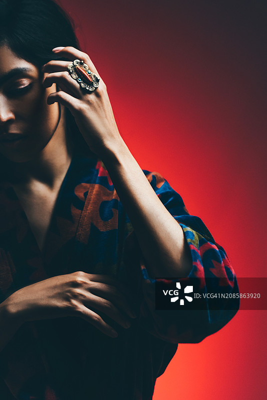 穿着色彩斑斓印花罩衫的女人站在红色墙壁旁。图片素材