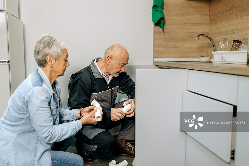 年长的水管工为中年妇女修理水槽图片素材