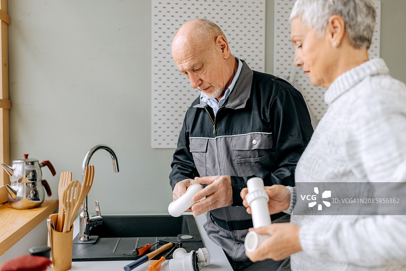 老年维修工与老年妇女在家中修理厨房水槽图片素材