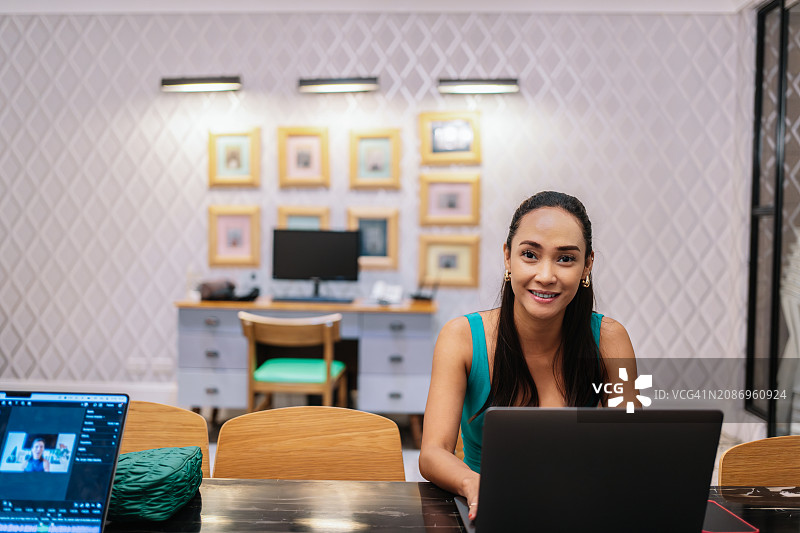年轻的亚洲女性坐在电脑前，微笑地看着镜头图片素材