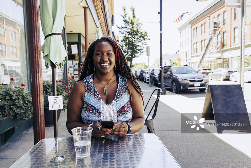 阳光明媚的日子里，坐在户外咖啡馆的快乐年轻女人图片素材