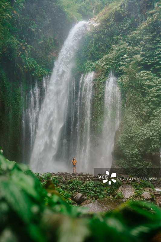 在丛林徒步旅行中，站在强大的热带瀑布附近的女人图片素材