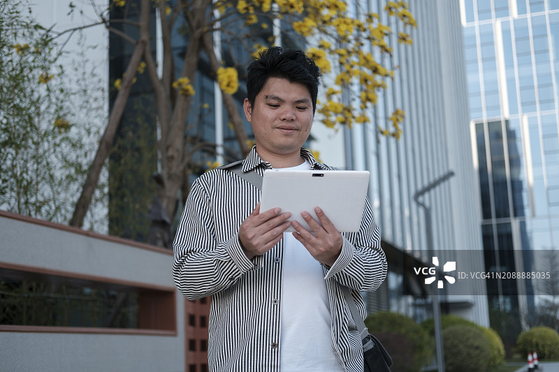 在办公楼下使用平板电脑的面带微笑的商人图片素材