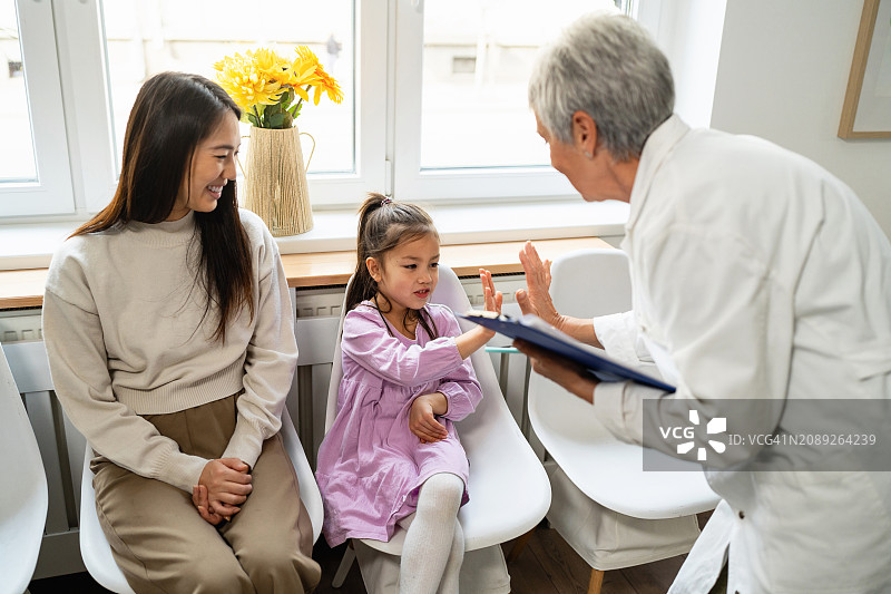 年长的白人女儿科医生在大厅与一名日本裔女孩及其母亲击掌图片素材
