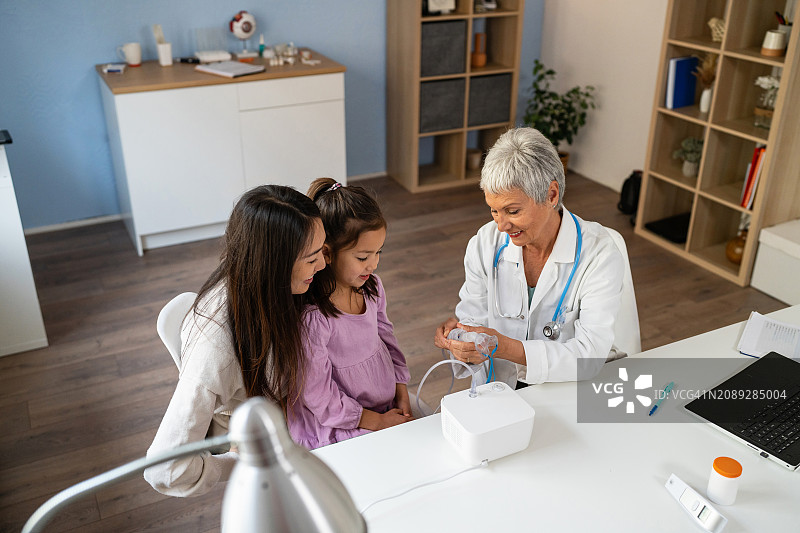 日本女孩接受雾化器治疗，来自年长的白人女儿科医生图片素材