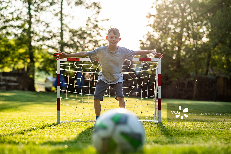 男孩在草地上踢足球，站在球门前防守图片素材