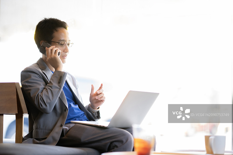 在咖啡店使用笔记本电脑和智能手机的年轻男商人图片素材